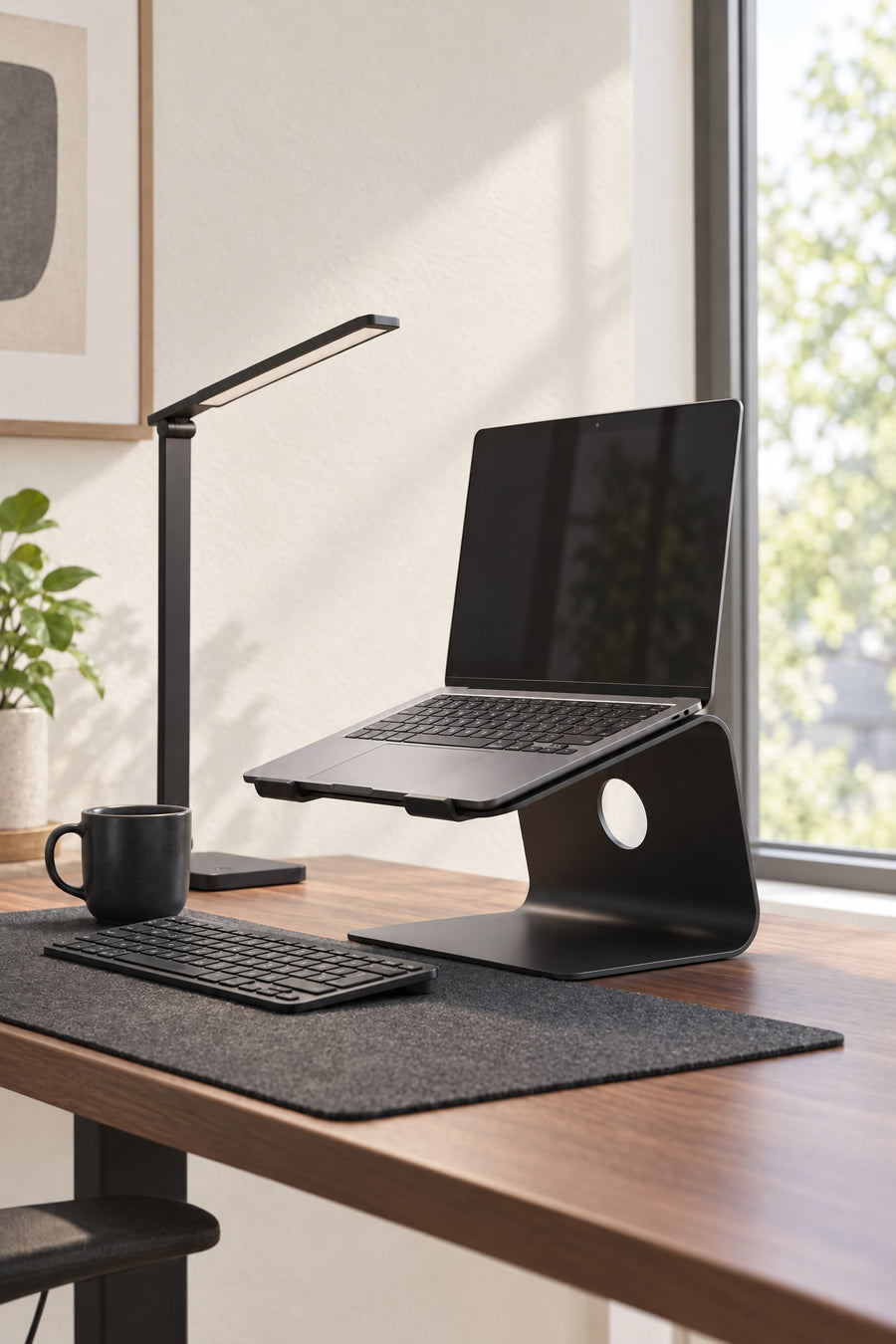 Soporte para notebook, lámpara, teclado y alfombrilla de fieltro sobre un escritorio de madera