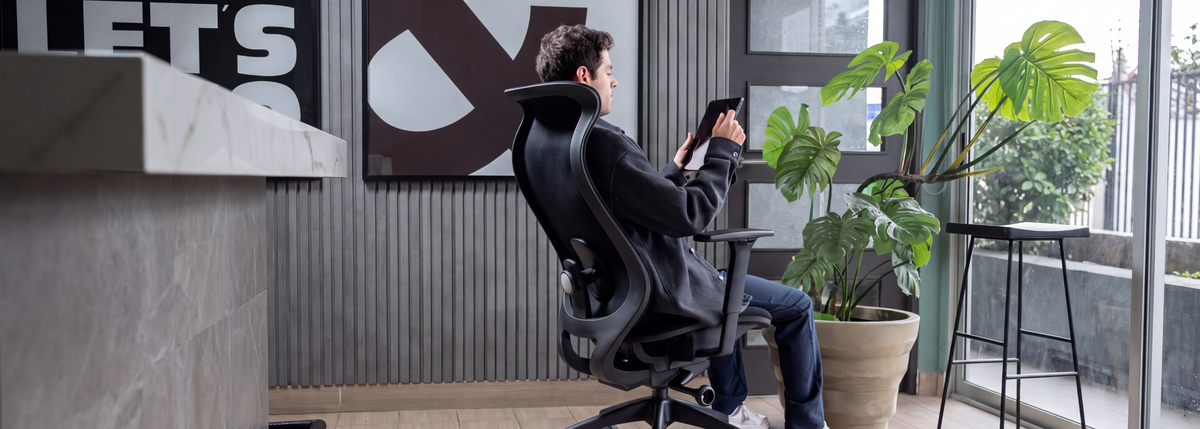 Hombre recostado en una silla ergonómica negra Modernismo revisando una tablet en una oficina moderna